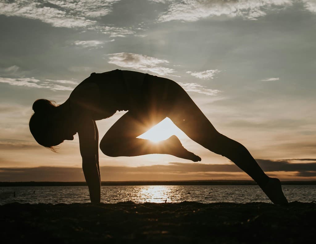 Silhouette de femme en posture de yoga face au soleil couchant sur la plage